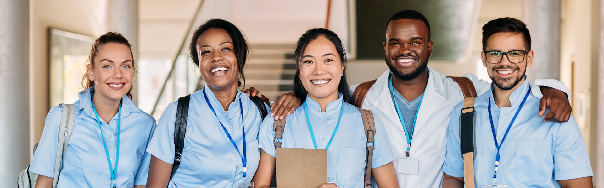 Multi0ethnic group of happy medical and nursing students standing in a hallway at medical university and looking at camera